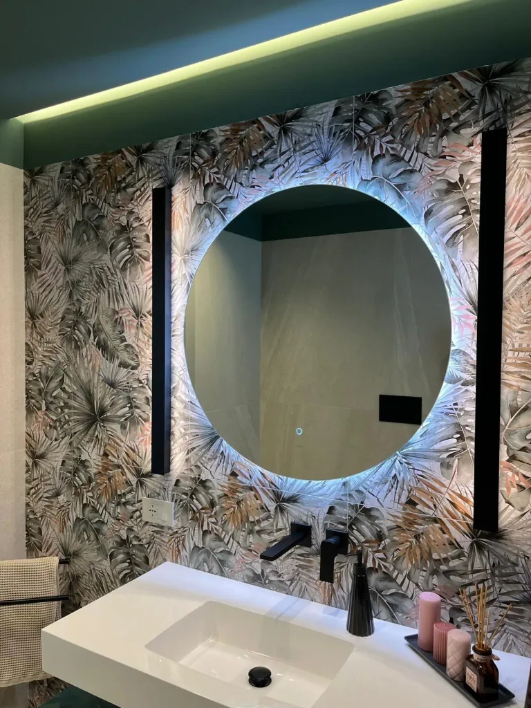 Bagno con carta da parati tropicale, specchio tondo retroilluminato e barre LED verticali