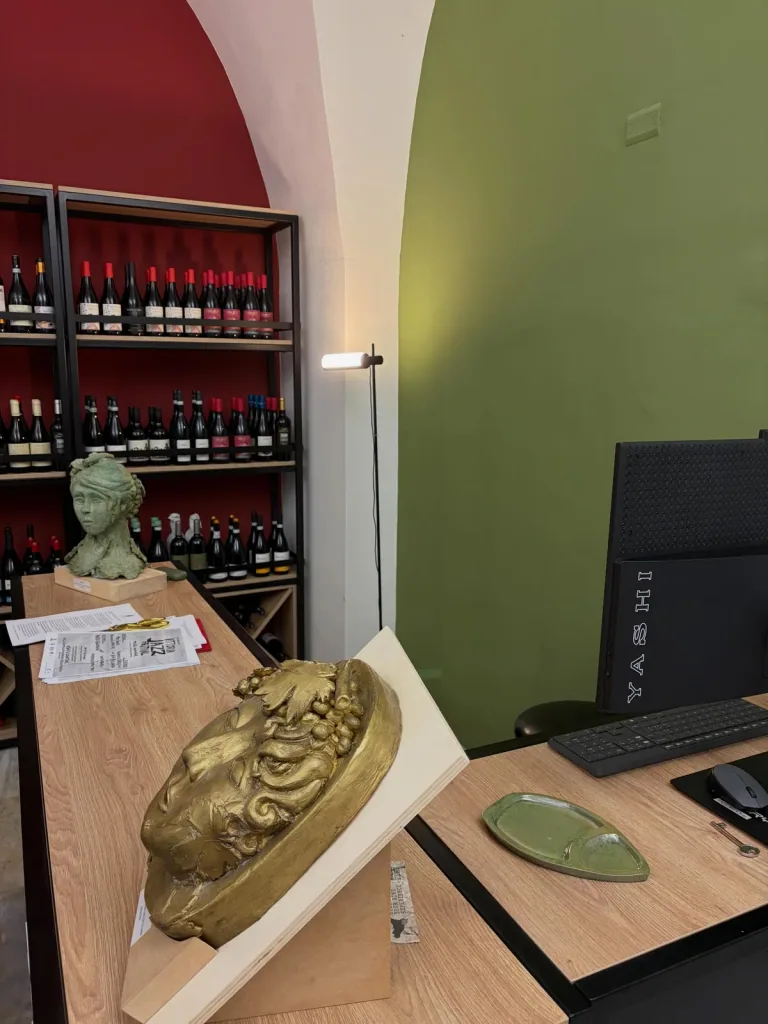 Scaffali di vini illuminati accanto a una parete rossa e a un arco verde
