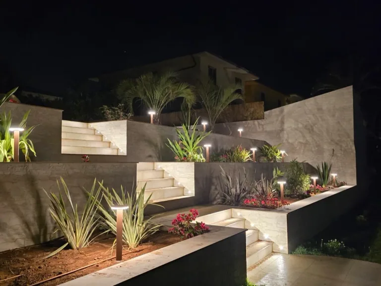 Giardino a terrazze di notte con paletti in corten accesi lungo le aiuole e le scale