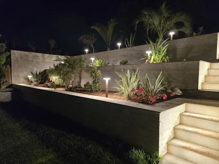 Aiuole con agavi e fiori rossi illuminate dai paletti in corten