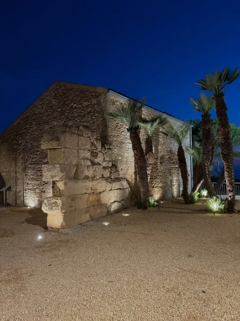 Edificio in pietra del museo di Kamarina illuminato dal basso di notte, tra le palme
