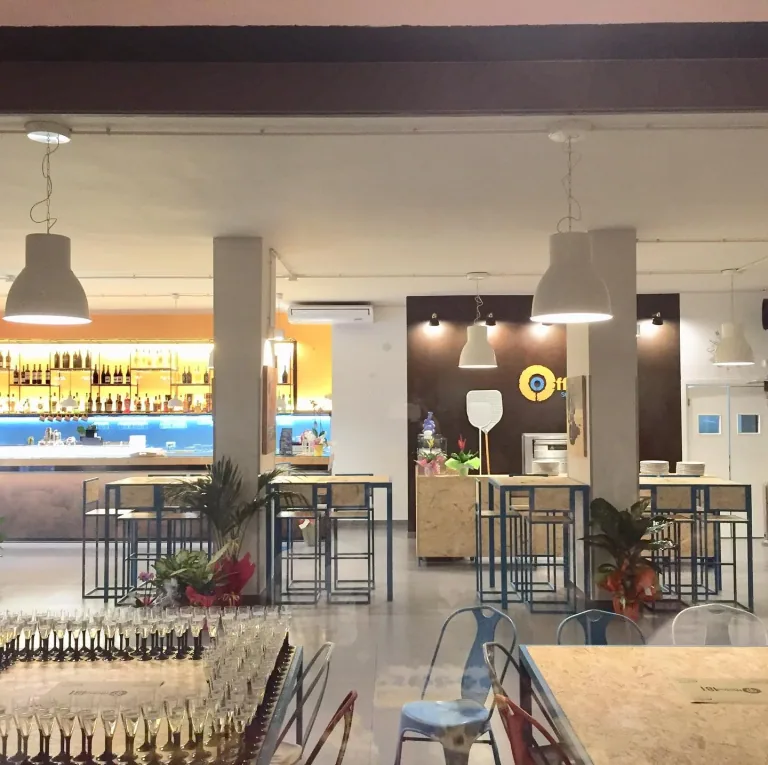 Sala del locale Officina 181 con sospensioni sopra i tavoli e il bancone illuminato sul fondo