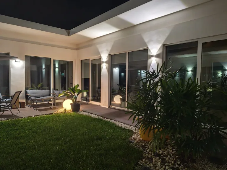 Patio di una villa di notte con applique a muro e lampade a sfera accese sul prato