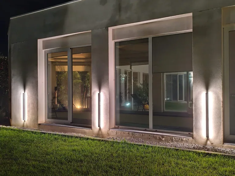 Facciata con vetrate e barre LED verticali accese sul prato