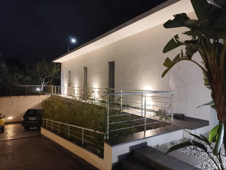 Lato della villa con applique a muro accese e la rampa d’ingresso