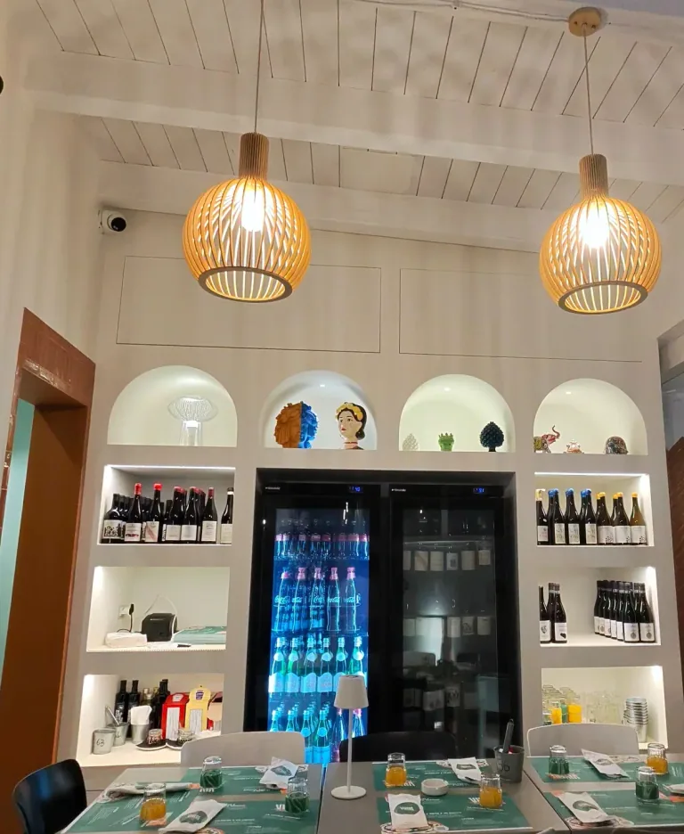 Sala della pizzeria con sospensioni in legno intrecciato sopra i tavoli e scaffali illuminati